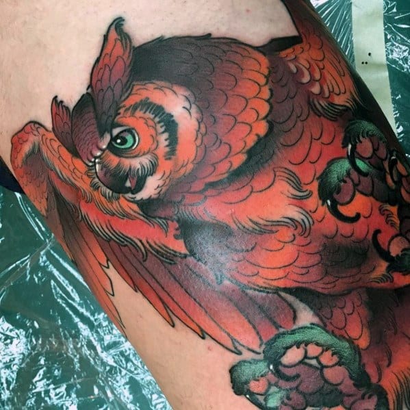 Neo-traditional owl tattoo in vibrant orange tones, featuring bold outlines, intricate feather details, and a fierce gaze in flight.