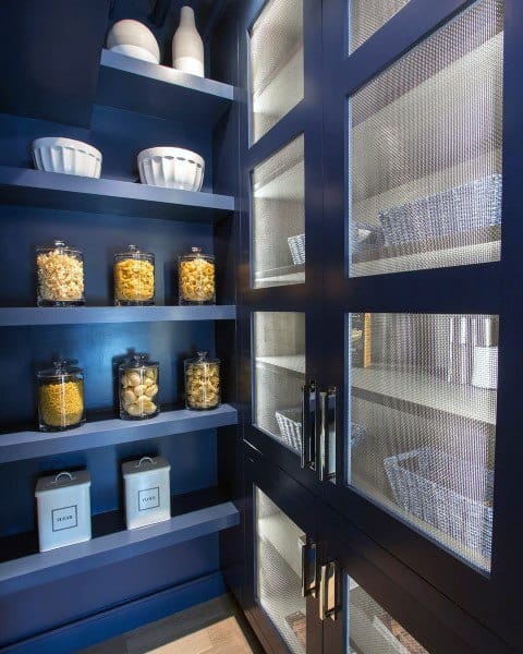 Dark blue pantry with mesh cabinet doors and neatly arranged jars and baskets.