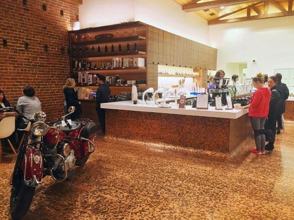 Cafe with penny tile flooring, modern bar counter, brick accent wall, and vintage motorcycle display.