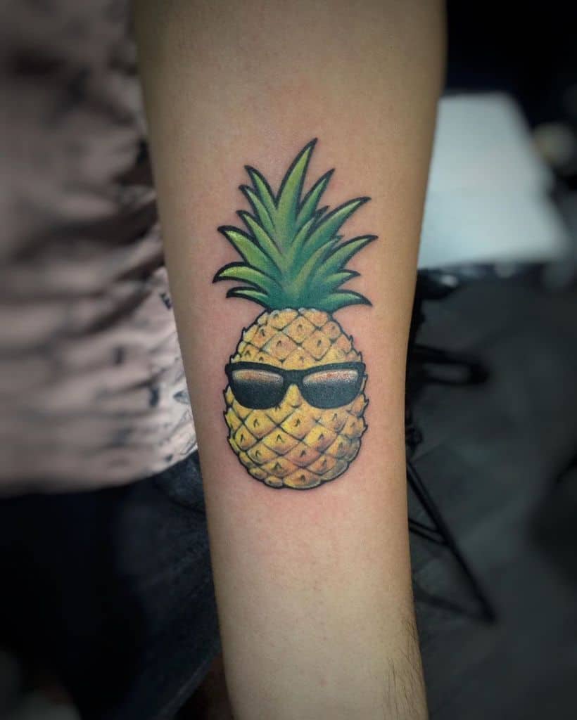 A colorful tattoo of a pineapple wearing black sunglasses, blending tropical and cool vibes in a fun and playful design on the forearm.