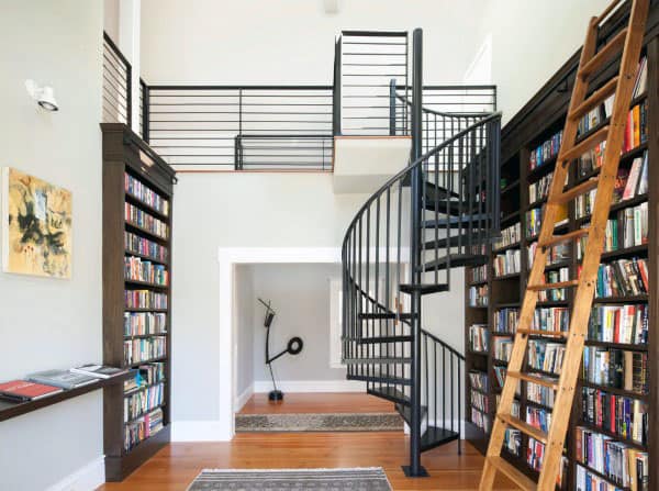 A home library with tall bookshelves, a spiral staircase, a wooden ladder, and modern art graces the walls
