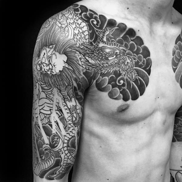 Black and grey Raijin shoulder and chest tattoo featuring fierce dragon, storm clouds, and dynamic Japanese linework.