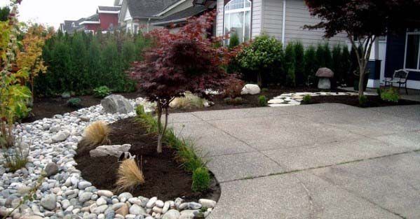 Stylish river rock landscaping along a curved driveway, featuring plants, trees, and clean, modern pathways