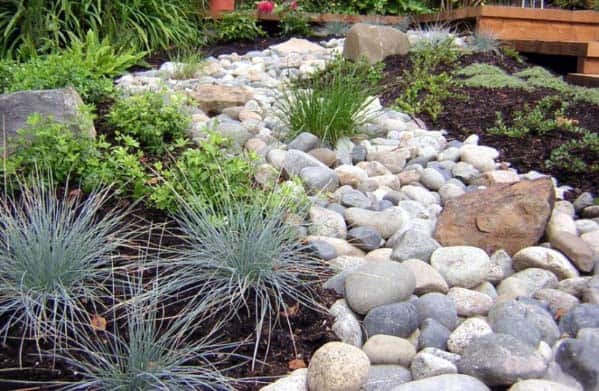 River rock landscaping with a mix of small and large stones, accented by vibrant greenery and plants for a natural, rustic look