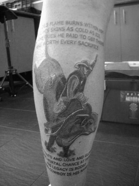 Black and grey tattoo of a bull rider mid-ride, featuring detailed shading, motion effects, and rodeo-themed text above and below the design.