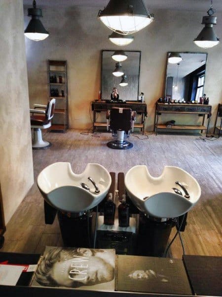 Rustic barbershop with wash basins, large mirrors, and industrial lighting fixtures.