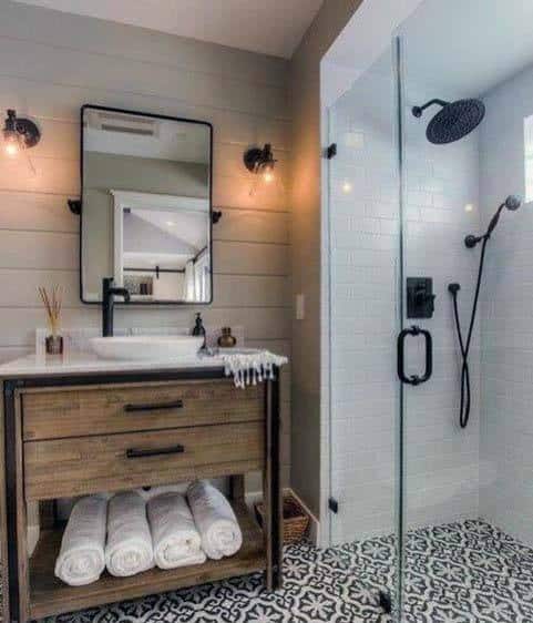 Rustic bathroom with wood vanity, round mirror, glass shower, and patterned tile floor