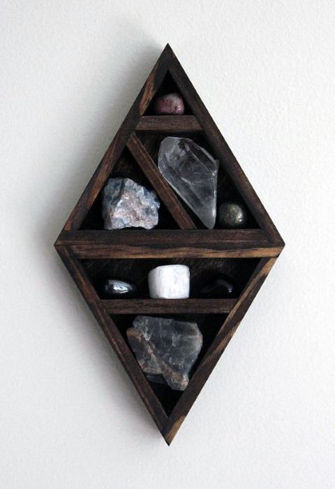 Diamond-shaped wooden shelf holding various crystals against a white wall.