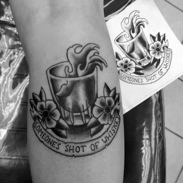 Black and grey shot glass tattoo with liquid splashing out, floral details, and a banner reading "Someone's Shot of Whiskey" for a bold design.