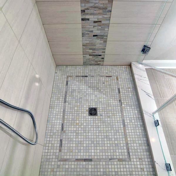 Beige and gray mosaic tile shower floor with central drain, glass door on the side
