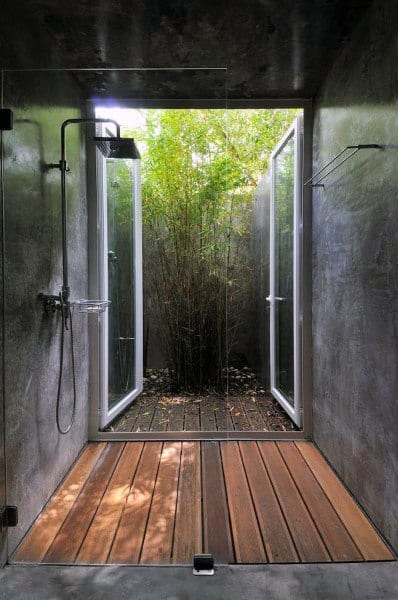 Modern shower with glass doors opens to a bamboo garden, boasting wooden flooring and sleek fixtures