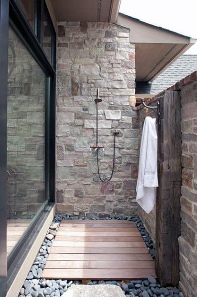 Outdoor shower with stone walls, a wooden floor, and a towel hanging on a rustic wooden shower panel
