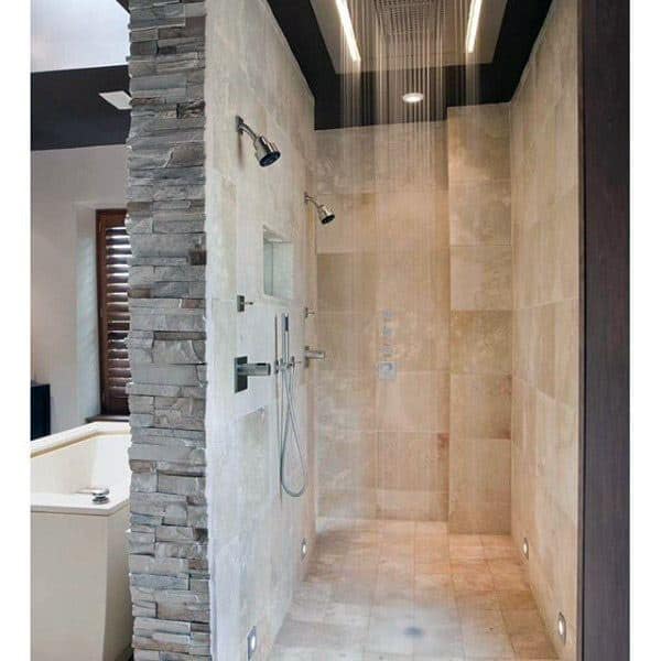 Modern shower with stone and beige tiles, ceiling rain showerhead, and wall-mounted shower controls