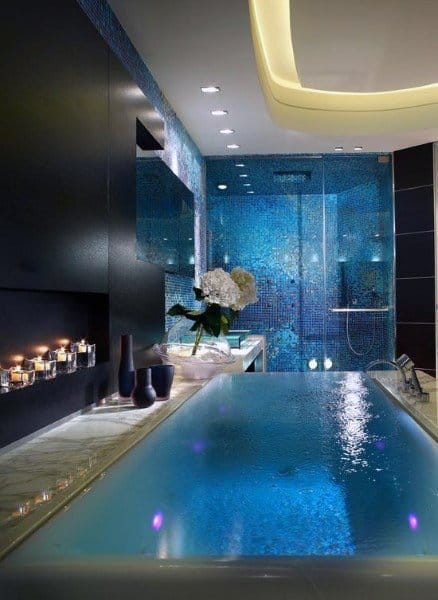 Luxurious bathroom with a blue-tiled wall, backlit bathtub, scented candles, and a sleek modern shower