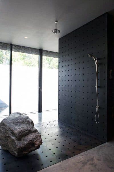 Modern shower with a dark, textured wall, ceiling rain showerhead, and a large rock near tall windows