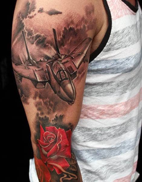 Arm tattoo of airplane flying among clouds with red rose below on bicep