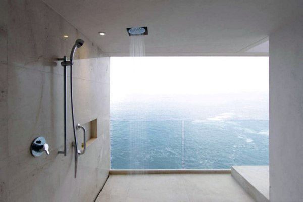Minimalist shower with ocean view through a large window, featuring a ceiling-mounted rain shower