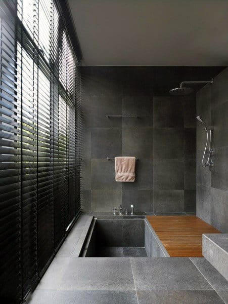 Modern bathroom with dark tiles, a glass shower wall, blinds, a towel rail, and a wooden bench in the shower area
