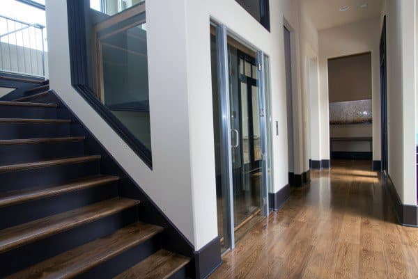 Modern interior featuring a glass elevator and sleek wooden staircase in a well-lit hallway