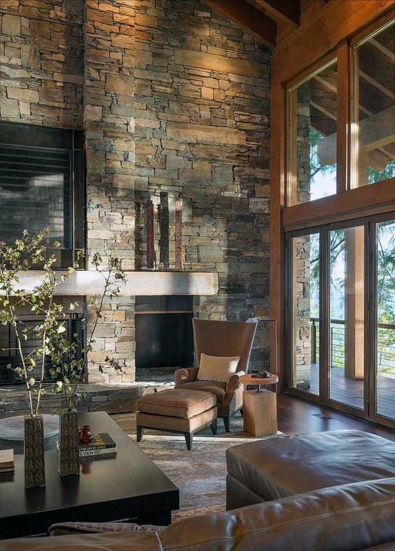Luxury living room with tall stacked stone fireplace, leather seating, and large glass windows.