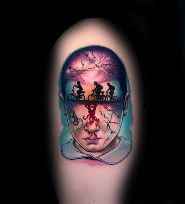 Colorful tattoo of Eleven’s face with Stranger Things silhouettes inside her mind, blending the Upside Down and real world in surreal detail.