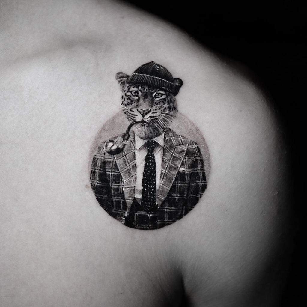 A creative tattoo of a jaguar dressed in a checkered suit and hat, with a pipe in its mouth, placed on the shoulder for a unique and stylish design.