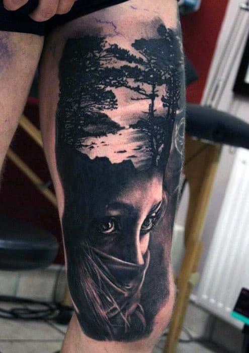 Surreal thigh tattoo of a veiled woman's eyes blending into an upside-down forest and sunset scene, creating a double exposure illusion.