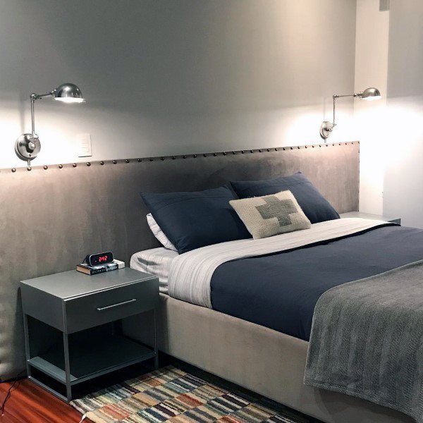 Modern bedroom with a gray bed, striped bedding, wall lamps, and a colorful rug on wooden flooring