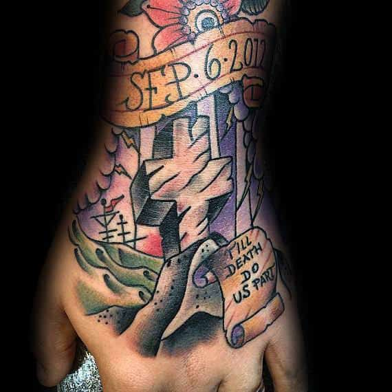 Colorful tattoo on the hand featuring a stone cross, two clasped hands, a scroll reading "Till Death Do Us Part," and the date Sep. 6. 2017.