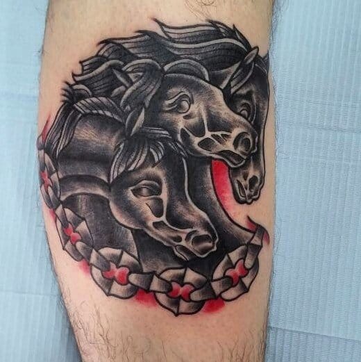 Traditional tattoo of three black horse heads with flowing manes, framed by a chain and red flower-like details.