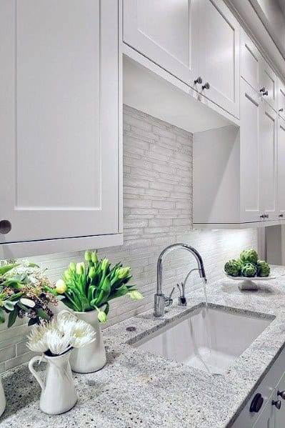 Bright kitchen with white cabinetry, a light stone backsplash, granite countertops, and fresh floral accents