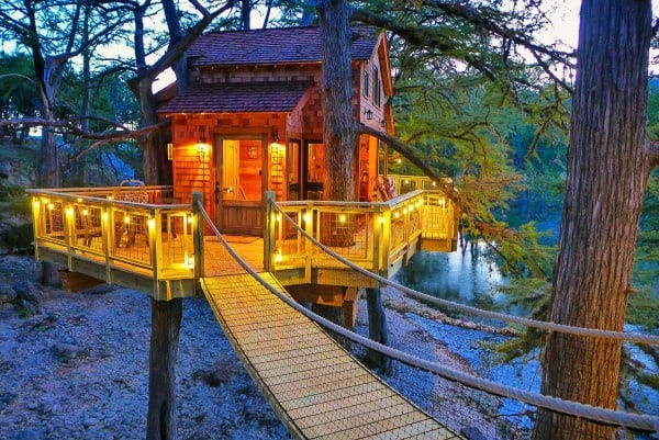 A cozy treehouse with glowing lights, surrounded by trees, connected by a rope bridge, near a calm river