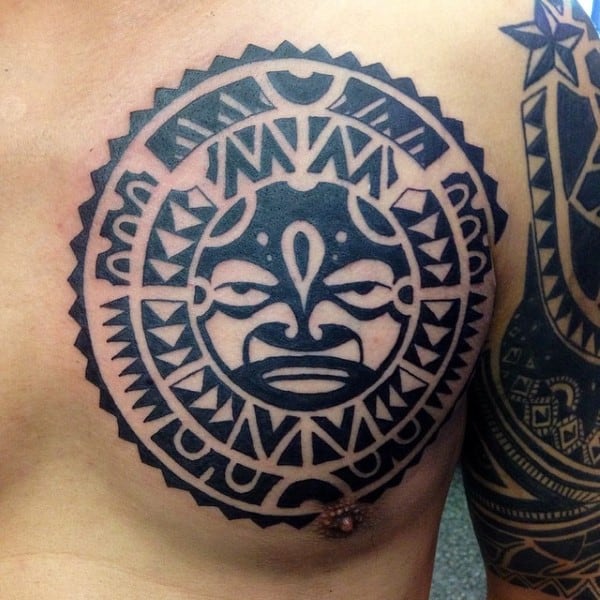 Tribal-style tattoo of a sun with a face on a chest near shoulder