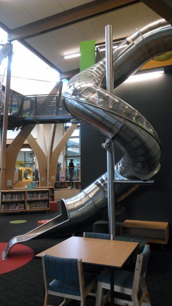 Indoor spiral slide amidst bookshelves and seating, creating a playful library retreat