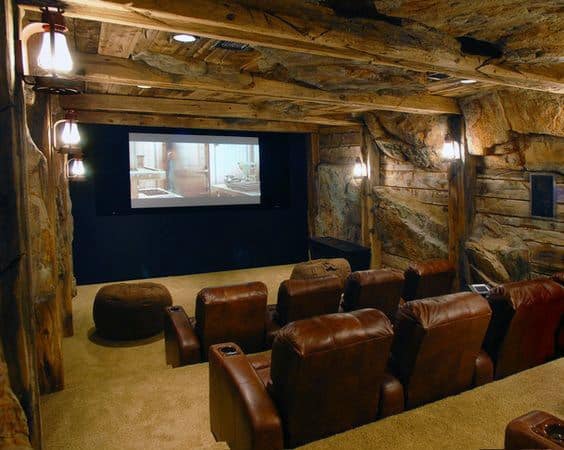 Rustic home theater with stone walls, wooden beams, cozy leather seating, and a large screen displaying a film