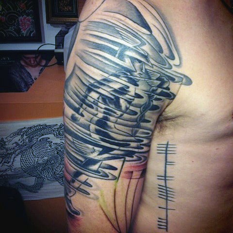 Distorted black and grey tattoo on upper arm, with lines on the side of the chest
