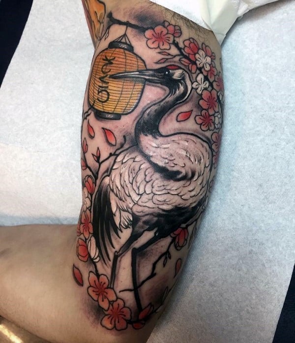 Inner arm tattoo featuring a detailed crane surrounded by cherry blossoms, falling petals, and a glowing Japanese lantern with fine shading