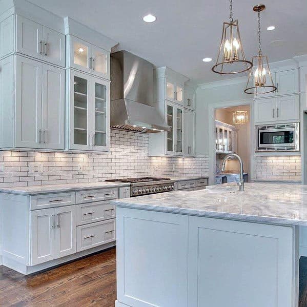 White kitchen with marble countertops, subway tile backsplash, and pendant lighting.