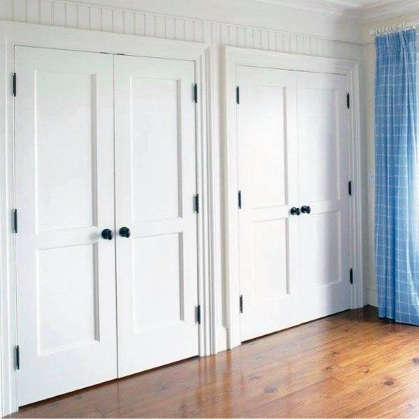 Two white closet doors with black knobs in a room featuring wooden floors and a blue checked curtain