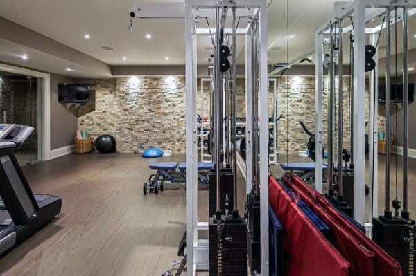 Home gym with exercise equipment, treadmill, resistance machines, and a mirrored wall; stone accent wall adds warmth