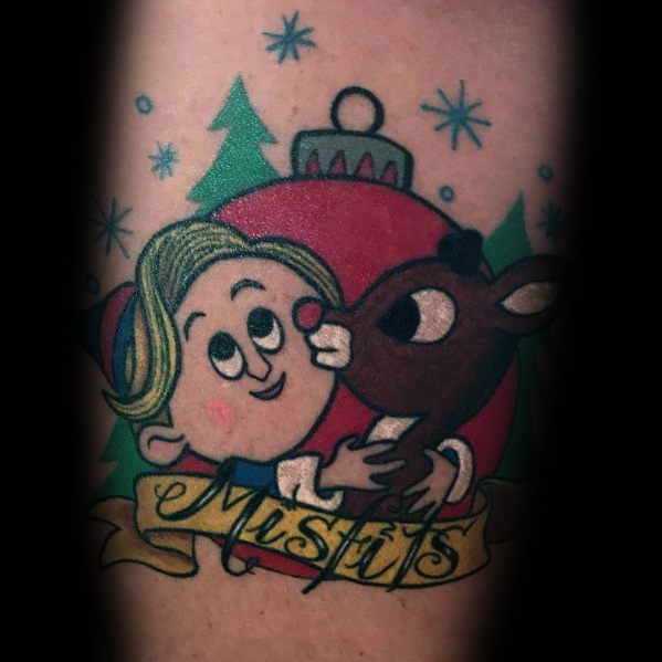Christmas tattoo featuring Hermey the Elf and Rudolph the Red-Nosed Reindeer in front of a festive ornament, with a "Misfits" banner below.