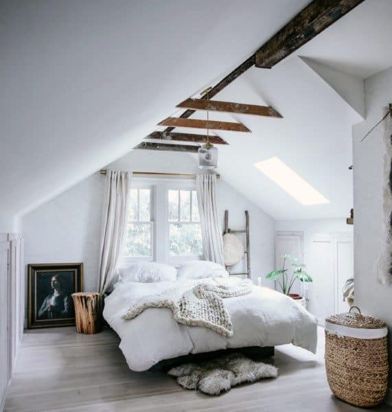 Cozy attic bedroom with white bedding, exposed beams, and a woven basket near a plant by the window