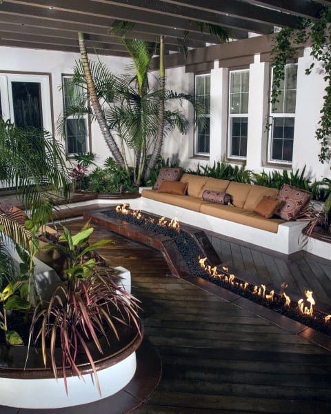 Backyard with tropical plants, wooden deck, built-in seating, and a modern linear fire feature.