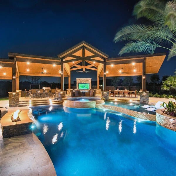 Luxury backyard with illuminated pool, hot tub, covered pavilion, and outdoor seating area.