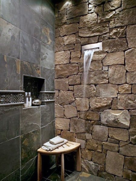 Stone wall shower with waterfall feature, bench, and toiletries elegantly displayed on a shower shelf