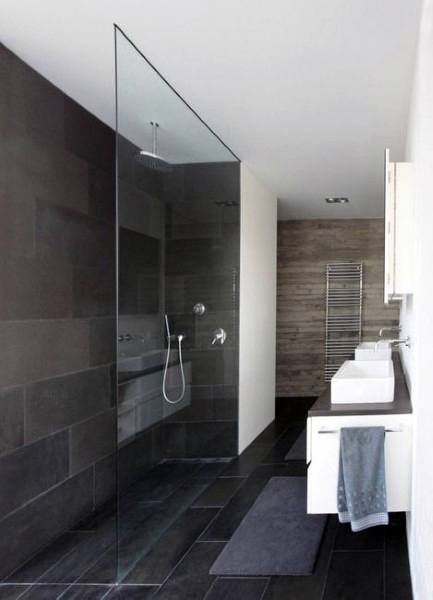 Modern bathroom with a glass shower, dark tiles, dual sinks, and a towel rack