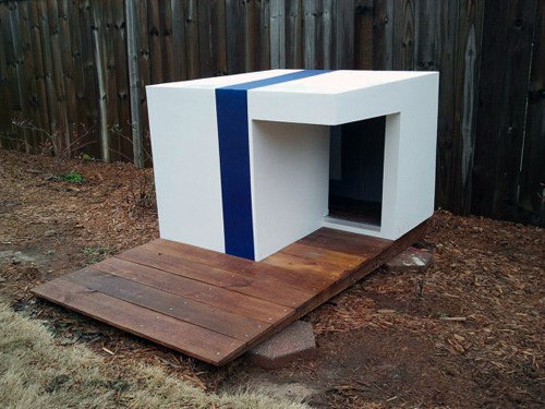 A modern white doghouse with a blue stripe and wooden deck