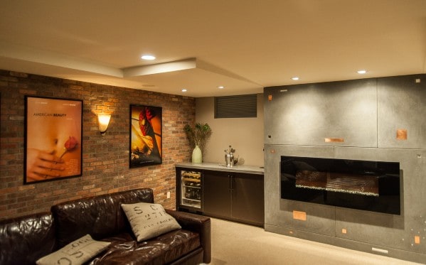 Cozy basement man cave with leather sofa, framed posters, mini bar, and modern fireplace