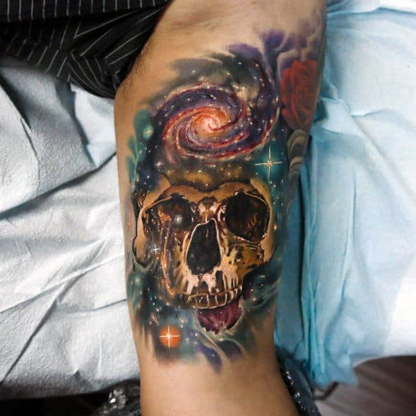 Colorful galaxy-themed tattoo featuring a skull beneath a swirling nebula and stars, symbolizing cosmic mystery, life, death, and the universe.