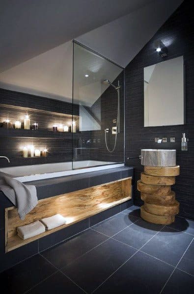Modern bathroom with a glass shower, lit candles, wooden sink, and shelf stacked with folded towels